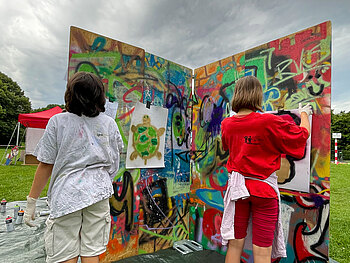 Zwei Jugendliche stehen vor einer Stellwand mit Graffitis.