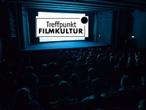 Dunkler Kinosaal mit Schülerpublikum vor der hellen Leinwand, auf der das Logo von Treffpunkt Filmkultur zu sehen ist