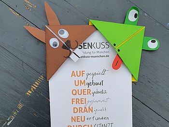 Vier aus Origamipapier gefaltete Lesezeichen, die wie Tiere gestaltet wurden, stecken an einem Faltblatt von Musenkuss München.