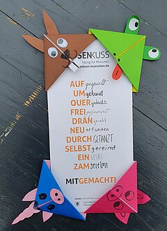 Vier aus Origamipapier gefaltete Lesezeichen, die wie Tiere gestaltet wurden, stecken an einem Faltblatt von Musenkuss München.