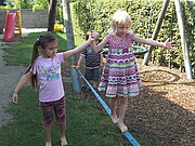 Ein Mädchen balanciert auf einer Slackline während eine andere sie stützt