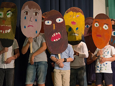 Kinder performen mit überdimensionalen Masken auf der Bühne
