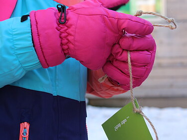 Ein Mädchen trägt Winterkleidung und hat einen Flyer an einem Bank um ihr Handegelenk gehängt