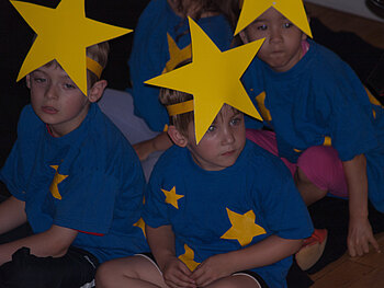 Kinder tragen blaue Tshirts, einen Stern auf dem kopf und weitere aufgeklaebt auf den ganzen Klamotten um wie die Flagge der EU auszusehen