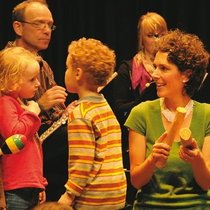 Kinder machen zusammen mit einer Lehrerin Musik mit Holzinstrumenten wie zum Beispiel Rasseln