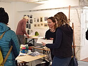 In einem Kunstatelier sind fünf Frauen, zwei von ihnen unterhalten sich, die anderen schauen sich im Atelier um.