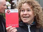 Eine Frau hält einen Flyer von Stattreisen in der Hand und lächelt in die Kamera