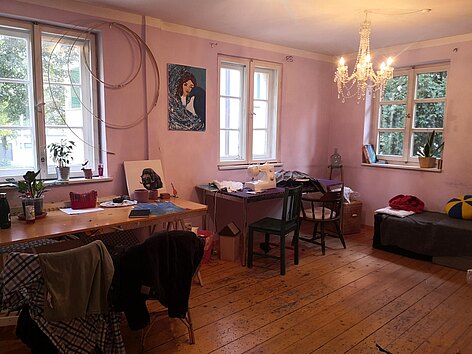 Atelier im Kür Kunstübungsraum. Die Wände sind rosa gestrichen und es gibt große Fenster. An der Wand stehen zwei Schreibtische. Auf einem steht eine Nähmaschine.