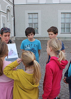Eine Frau zeigt einer Gruppe Kindern Skizzen von Ballkleidern
