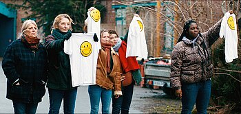 Mehrere Frauen halten jeweils ein weißes T-Shirt mit einem gelben Smilie darauf in die Höhe