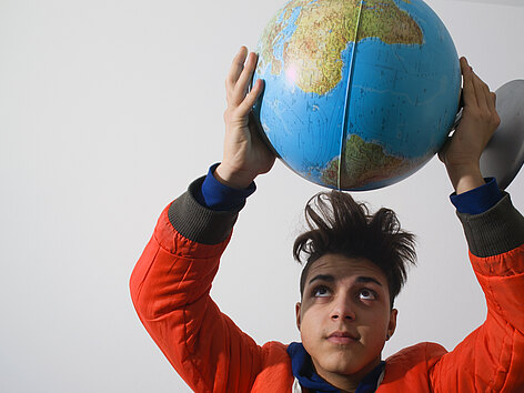 Ein Junge hält eine Plastik-Weltkugel über seinen Kopf und sieht zu ihr nach oben