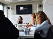 In einem Seminarraum nehmen vier Personen an einer Videokonferenz teil.
