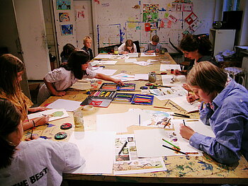 Kinder sitzen an einem langen Tisch und malen