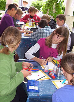 Mehrere Gruppen an Kindern malen und basteln an verschiedenen Tischen