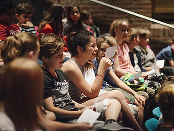 Eine Gruppe von Kindern sitzt in einem Saal und interagiert mit einem Medienpädagogen.