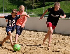 Zwei Kinder spielen mit ihrer Trainerin Ball in der Lilalu-Beacharea im Olympiapark