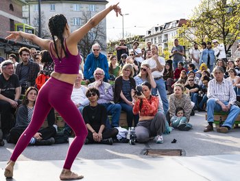 Eine junge Frau tanzt auf dem Platz am Kulturkraftwerk. Zuschauer sitzen daneben und schauen ihr zu.