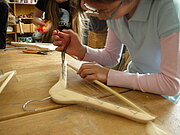 Zwei Jugendliche bearbeiten Holzkleiderbügel, um daraus ein Saiteninstrument zu bauen.