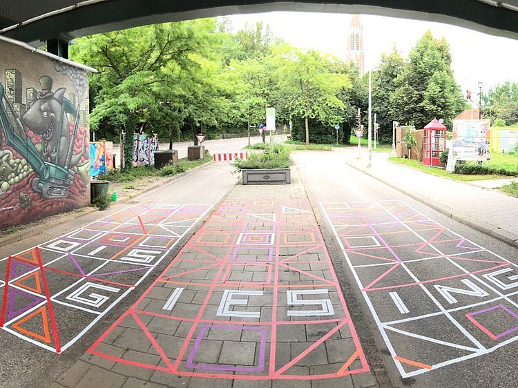 Der TAPE ART Künstler Rodewaldt hat mit bunten Klebebändern "OIS GIASING" auf die Bodenfläche der ehemaligen Bushaltestelle 58 geschrieben