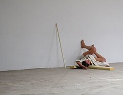 Performancekünstlerin liegt auf dem Boden mit den Füßen an die Wand gelehnt