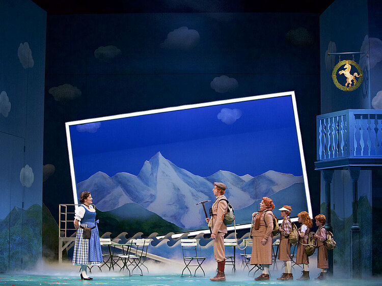 Bild aus der Operette Im weißen Rössl, vor einer Berglandschaft steht eine Familie von rothaarigen Wanderern mit drei Kindern