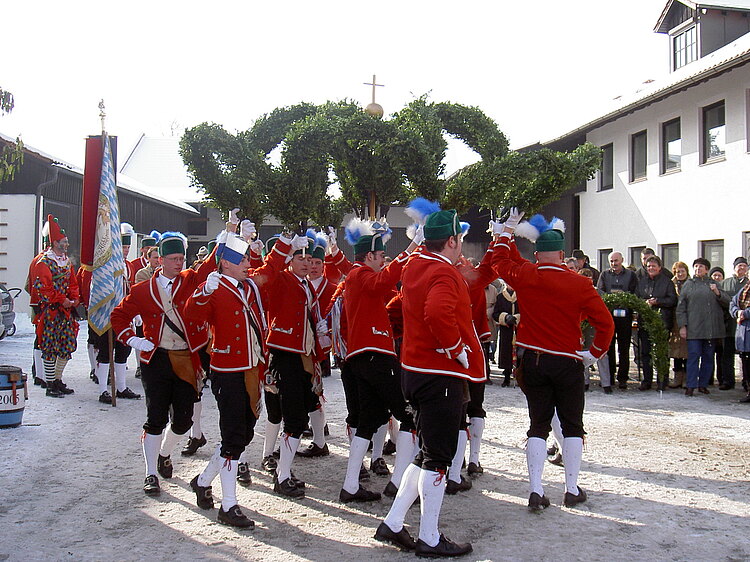 Eine Gruppen von Männern tanzt in traditioneller Kleidung und Ästen in den Händen