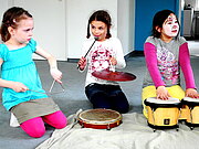 Drei Mädchen machen Musik mit Triangel, Schelle und Trommeln