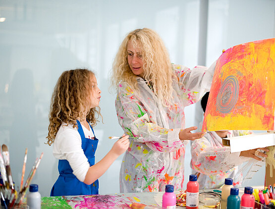 Frau zeigt einer jungen Malerin ihr Kunstwerk und redet darüber