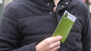 Teilnehmer hält einen Flyer der Stattreisen in der Hand und lächelt in die Kamera