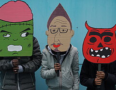 Drei Jungen halten sich überdimensionale Masken mit bunten Monsterköpfen ins Gesicht