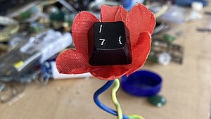 Aus Stoff, Draht und einer Tastaturtaste wurde eine rote Blume gestaltet.