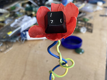 Aus Stoff, Draht und einer Tastaturtaste wurde eine rote Blume gestaltet.