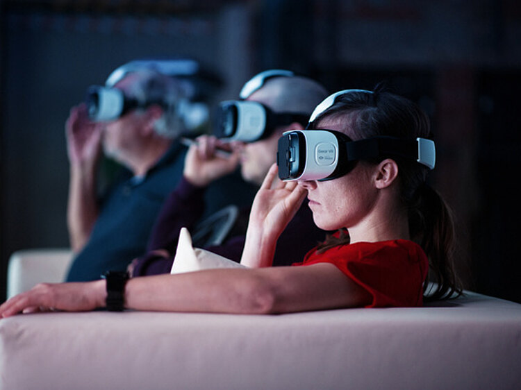 Drei Personen sitzen auf einer Couch und tragen Virtual Reality Brillen