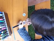 Ein Kind malt an einem Biertisch auf rundes Papier, neben ihm liegen noch Stifte und fertige Anstecker.