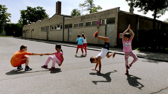 Mehrere Kinder tanzen im Freien auf einem Hof.  