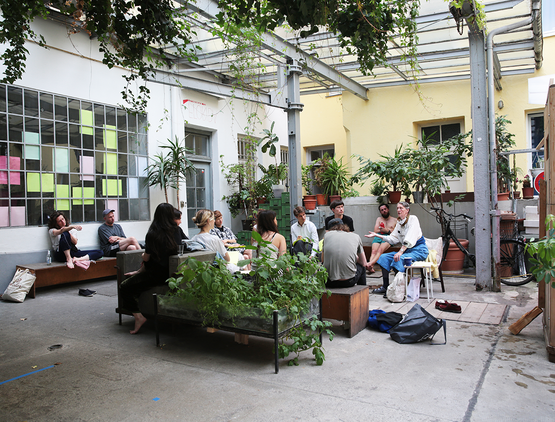 Leute sitzen im Hof des Kunstraums zusammen von Pflanzen umringt