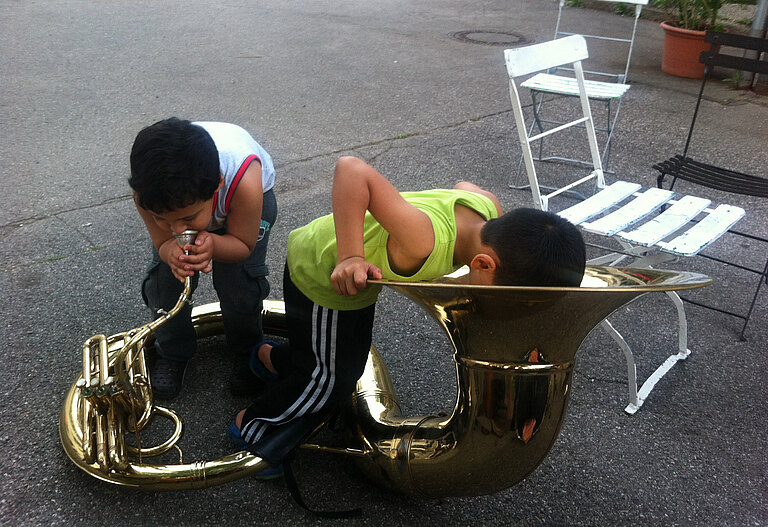 Zwei Kinder spielen mit einer großen Tuba.  