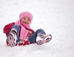 Ein Mädchen rutscht einen schneebedeckten Berg herunter