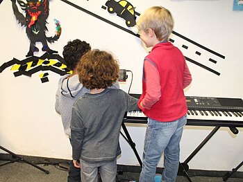 Drei Kinder stehen vor einem elektrischen Klavier