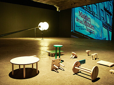 Ausstellung im Maximiliansforum mit Videoinstallationen und umgekippten Stühlen und Tischen