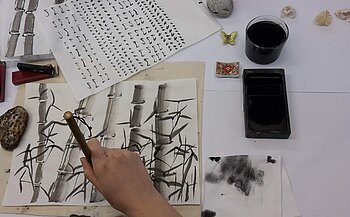 Eine Hand, die mit einem japanischen Pinsel und Tusche kleine Knoten an Bambusstangen malt.
