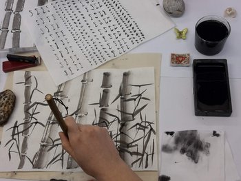 Eine Hand, die mit einem japanischen Pinsel und Tusche kleine Knoten an Bambusstangen malt.