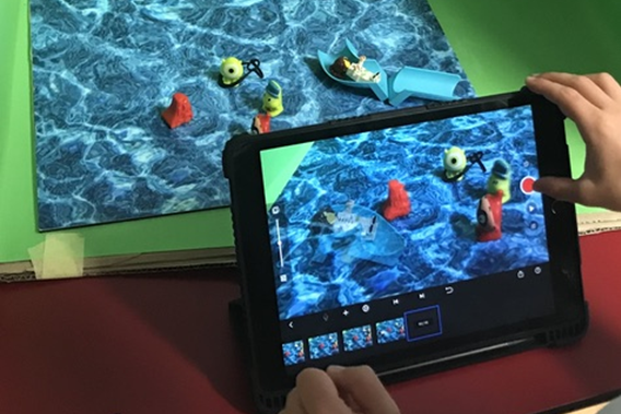 Zwei Hände fotografieren für einen Trickfilm mit einem Tablet eine Wasserszene, die in einer Greenbox eingerichtet wurde.